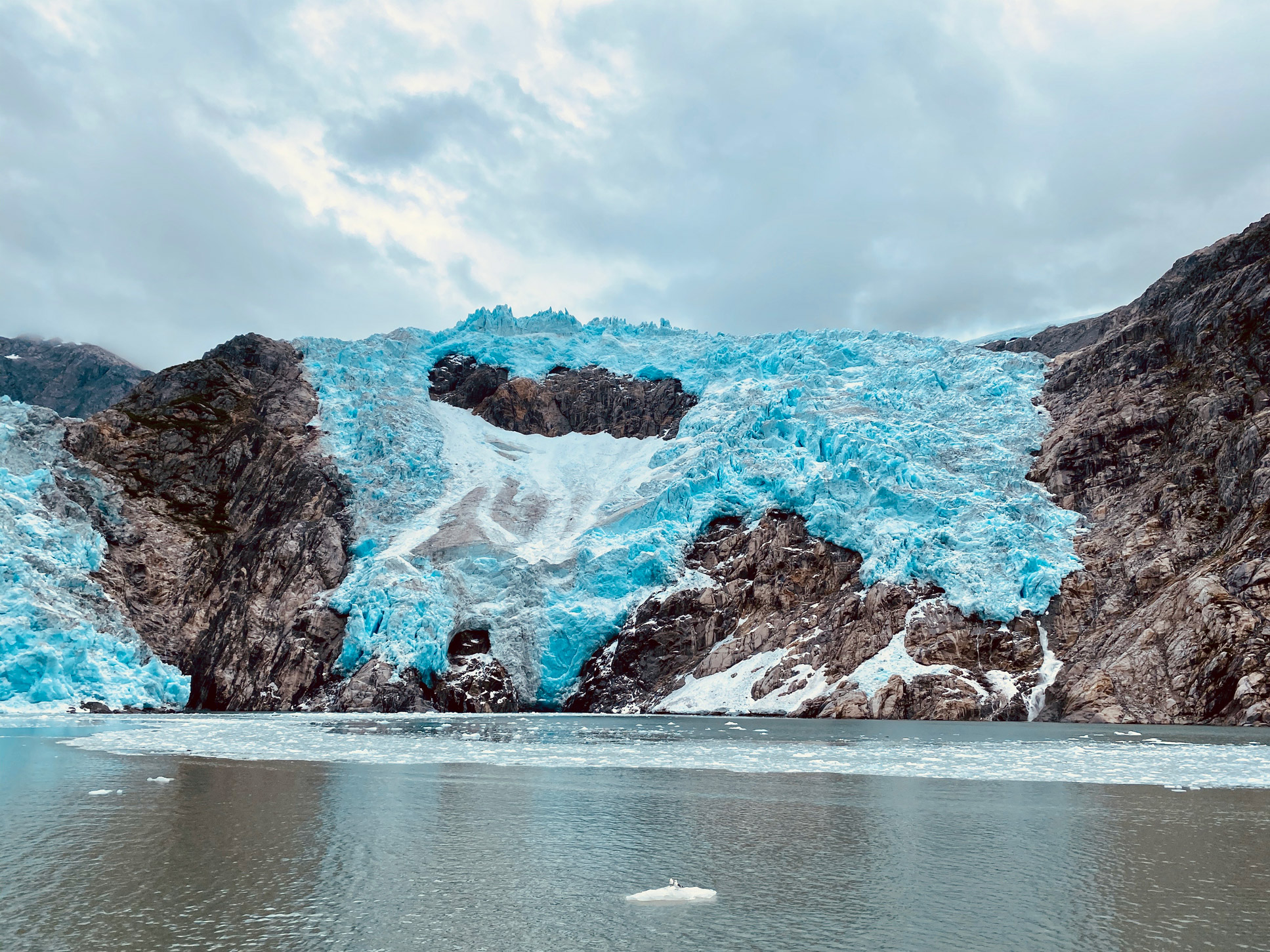 large cliffside in alaska covered in snow and ice by a frozen lake